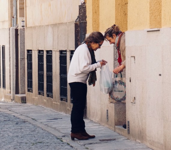 A photo of two women, one in her doorway and the other handing her a bag of groceries