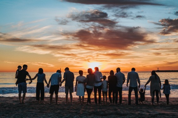 A group of people standing together on the shoreline of a beach at sunset.
