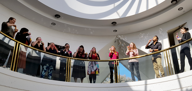Group picture of MHA staff blowing bubbles over a sunny atrium.