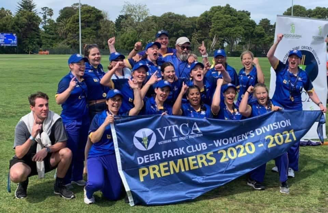 Group photo of Deer Park women's division cricket club holding a large, triangular premiers flag. The flag says: &quot;VTCA Deer Park Club - Women's Division Premiers 2020-2021&quot;
