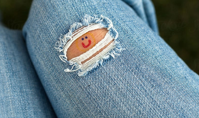 Close up image of the legs of someone wearing ripped jeans. The rip is just above the knee and a smiley face is drawn on the skin revealed by the rip
