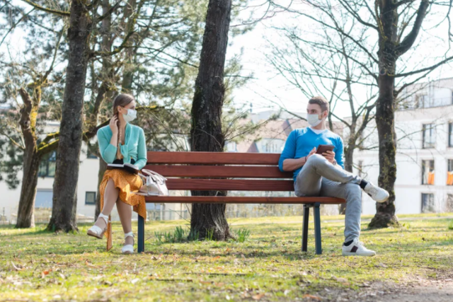 Picture of two people wearing masks on opposite sides of a bench.