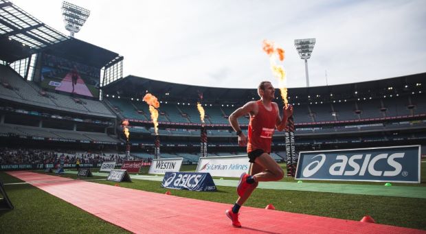 Person wearing red running in a stadium with flames shooting from poles in the background.