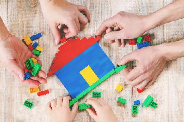 Three pairs of hands constructing a house out of lego.